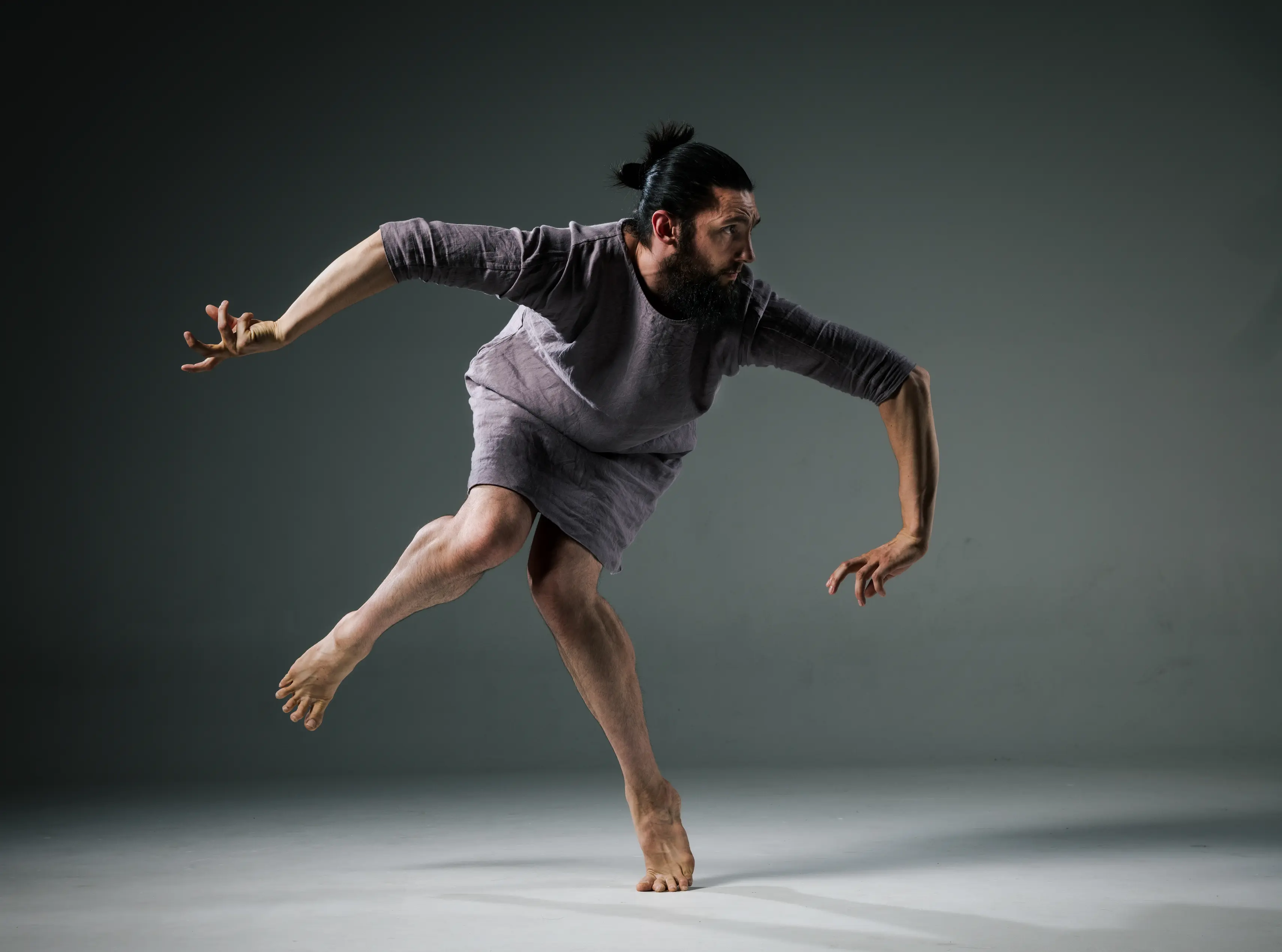 Samuel Hobbs forming an articulated pose on one leg while in an elegant purple dress.